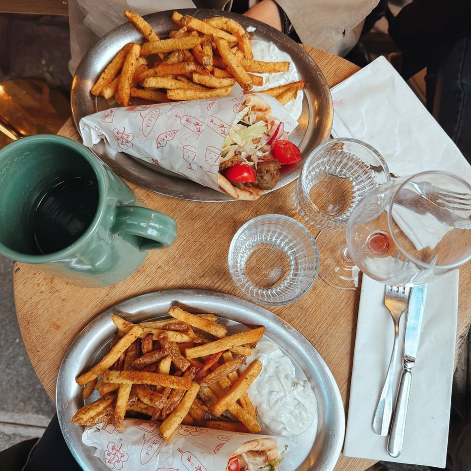 Közeli egy megpakolt gyros tálról fatálcán, a háttérben kosárnyi steakburgonyával.