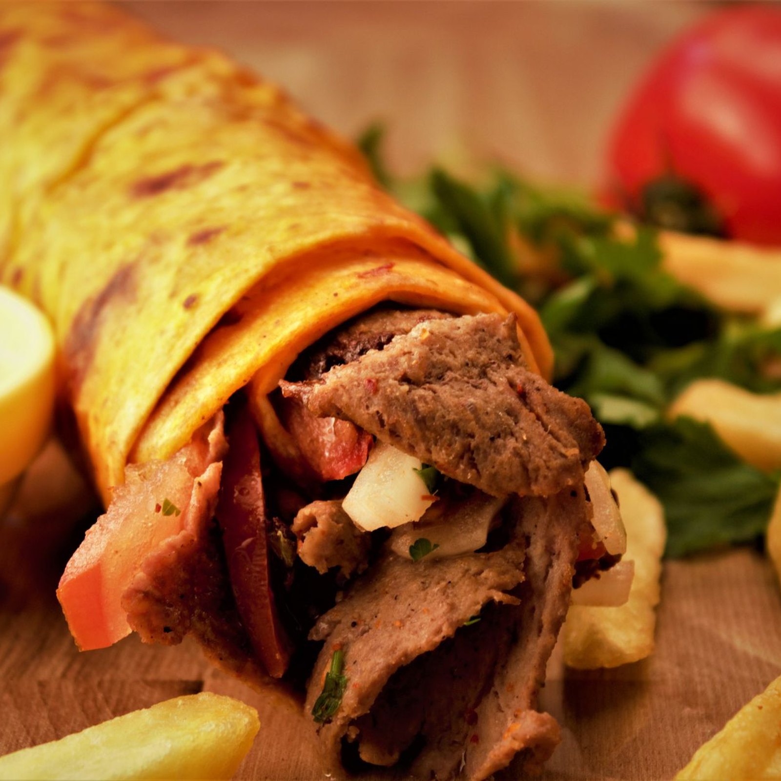 Felülnézet két megpakolt gyros pitáról, friss salátával, lilahagymával és tzatzikivel, fatálcán, rusztikus terítőn.