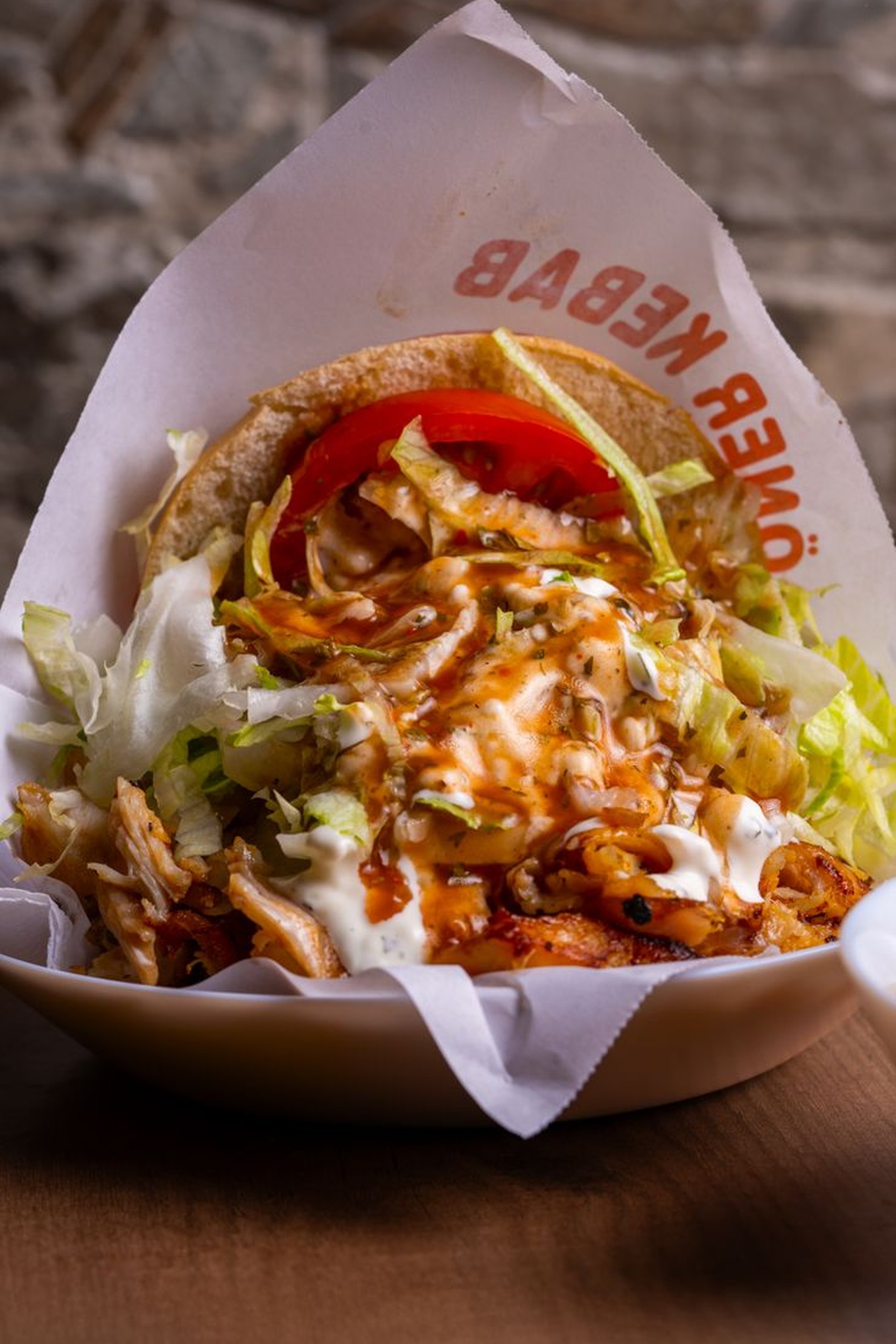 Kezek nyúlnak gyros pita és wrap felé, középen egy hideg üveges üdítő.
